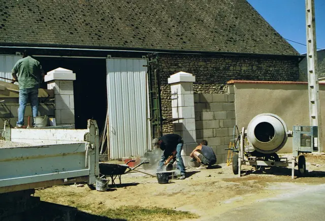 Préparation du mortier à la bétonnière devant une grange en pierre