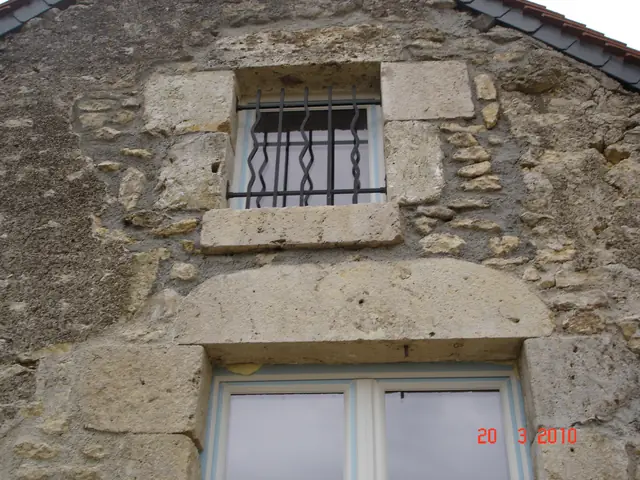 Façade en pierre restaurée avec fenêtre et soupirail à grille en fer forgé