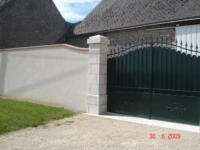 Mur de clôture enduit et pilier en pierre, vue d'angle avec portail vert