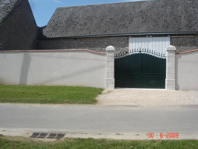 Vue d'ensemble d'un mur de clôture enduit avec portail et piliers en pierre