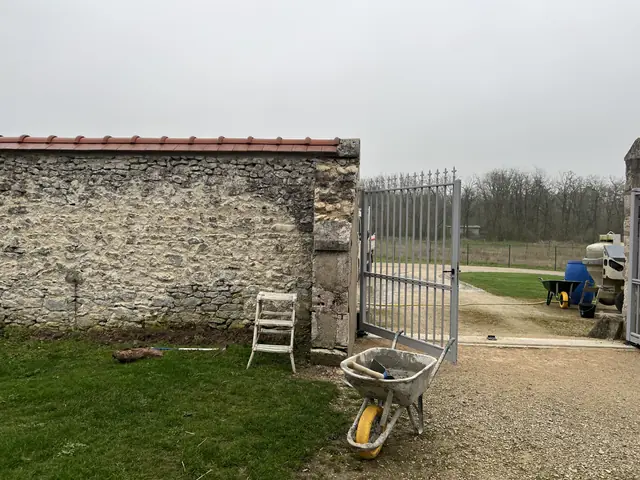 Mur de clôture en pierre avant rejointoiement, portail en fer